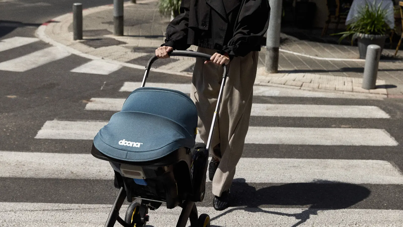 Parent pushing a Doona car seat stroller across a zebra crossing in stroller mode